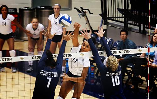 Freshman Aaliya Davidson spikes the match winning point over two Georgetown blockers. Kiana Robertson | Hatchet Photographer